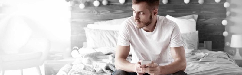 Man sitting on a bed with his phone