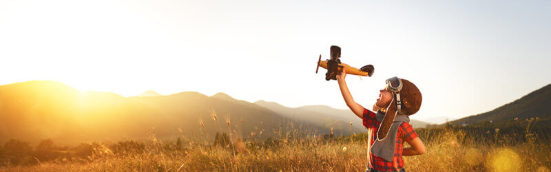 Banner - Kid playing with airplane in a open field at sunset